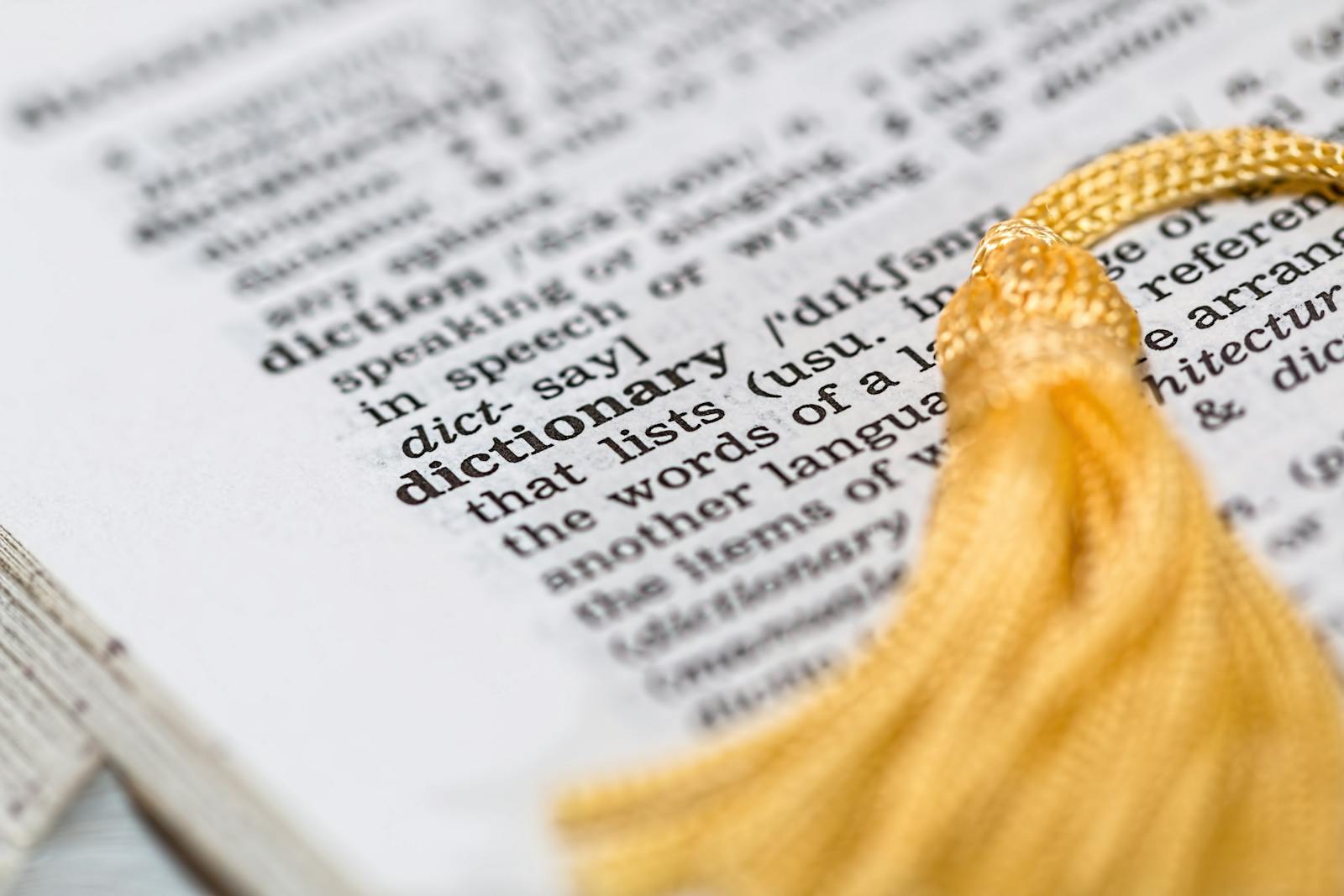 Close-up image of a dictionary page focused on the word 'dictionary' with a yellow tassel.