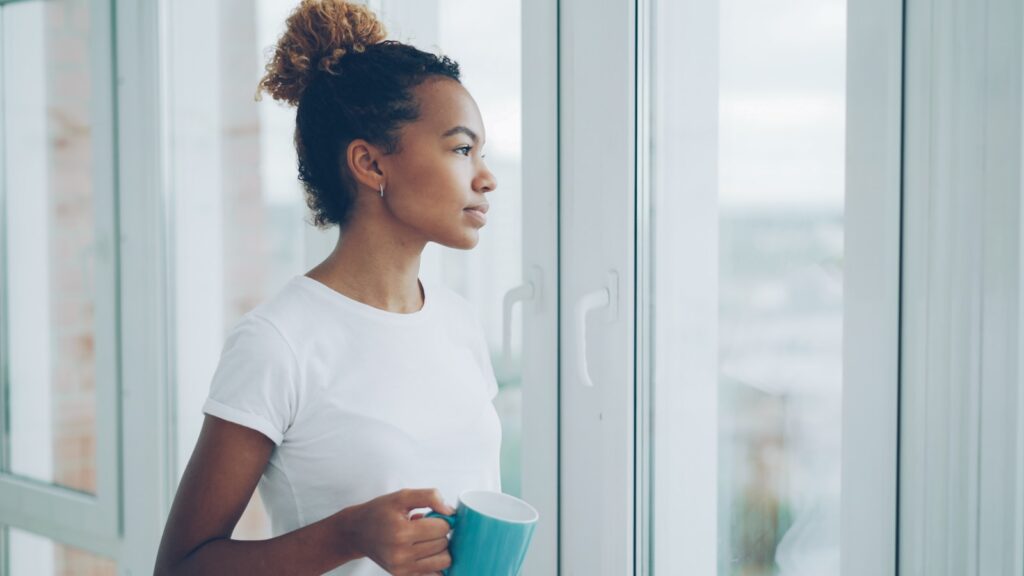Woman holding mug and looking out window.